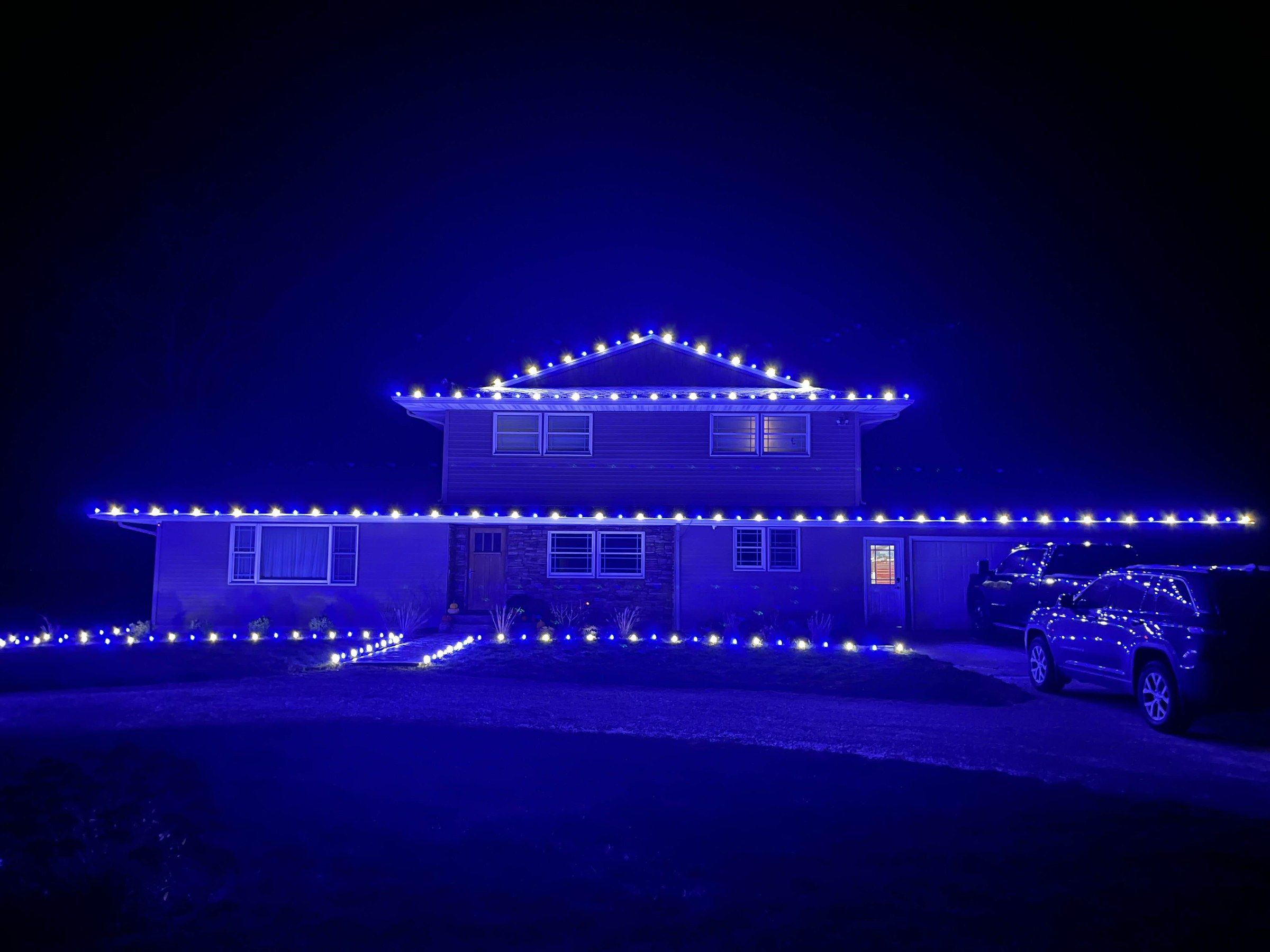 Split-level home with alternating blue and warm white Christmas lights along the roof and walkway