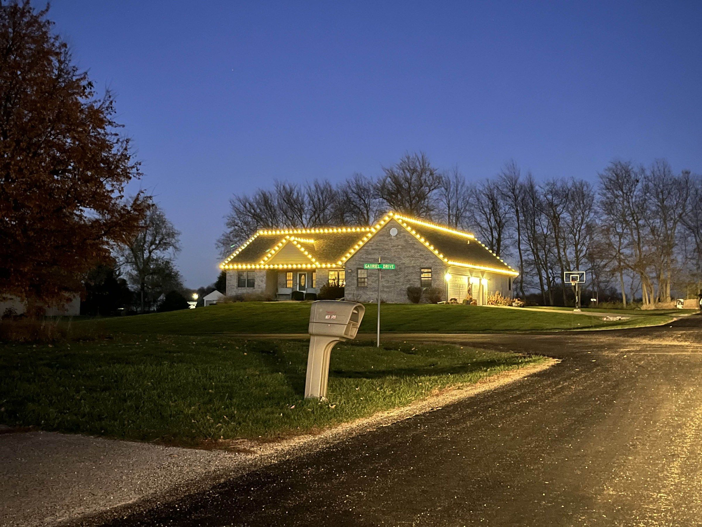 Brick ranch home at dusk with warm white C9 roofline Christmas lights on every peak