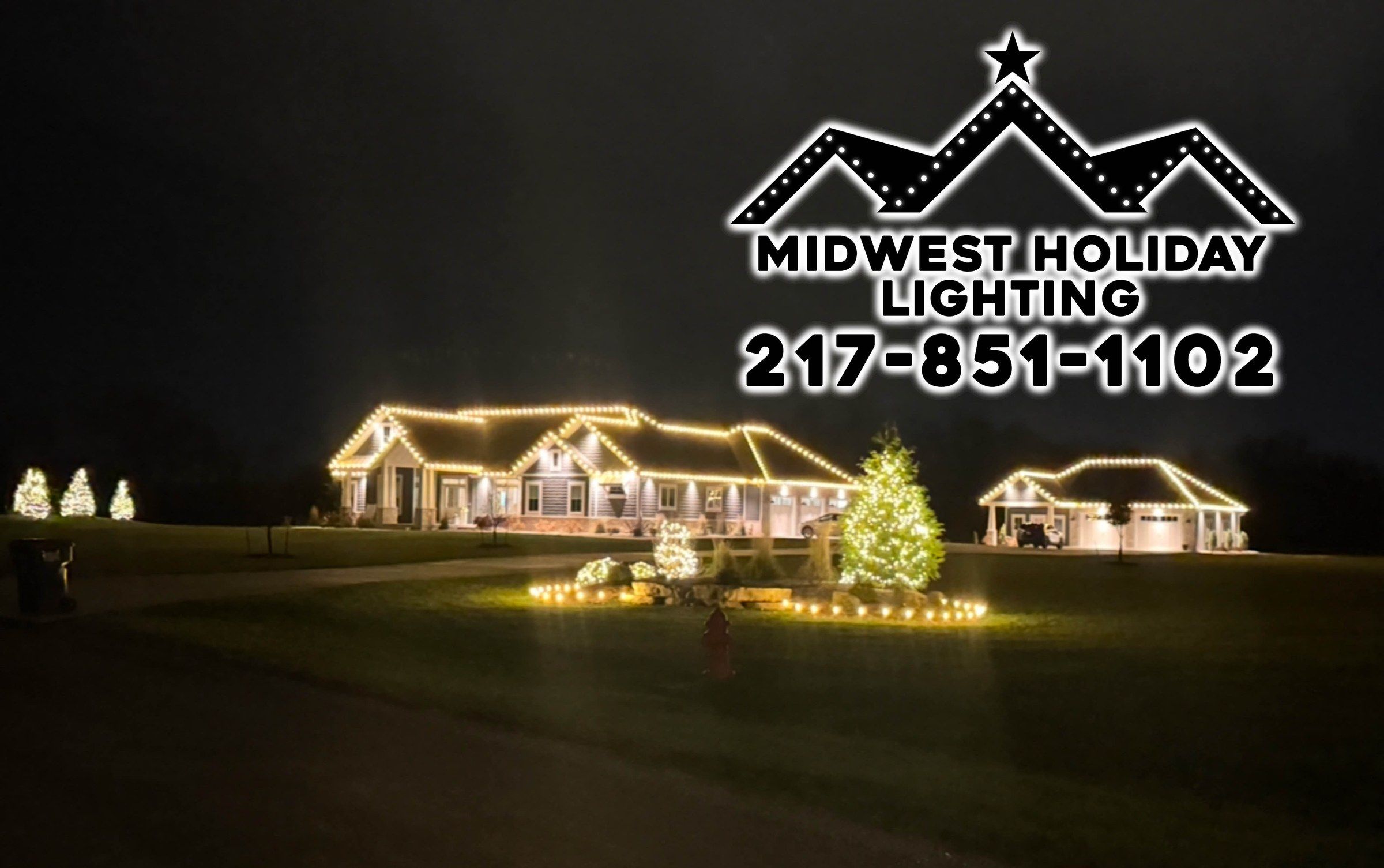 Ranch home and detached garage outlined in warm white Christmas lights with wrapped trees and lit evergreens