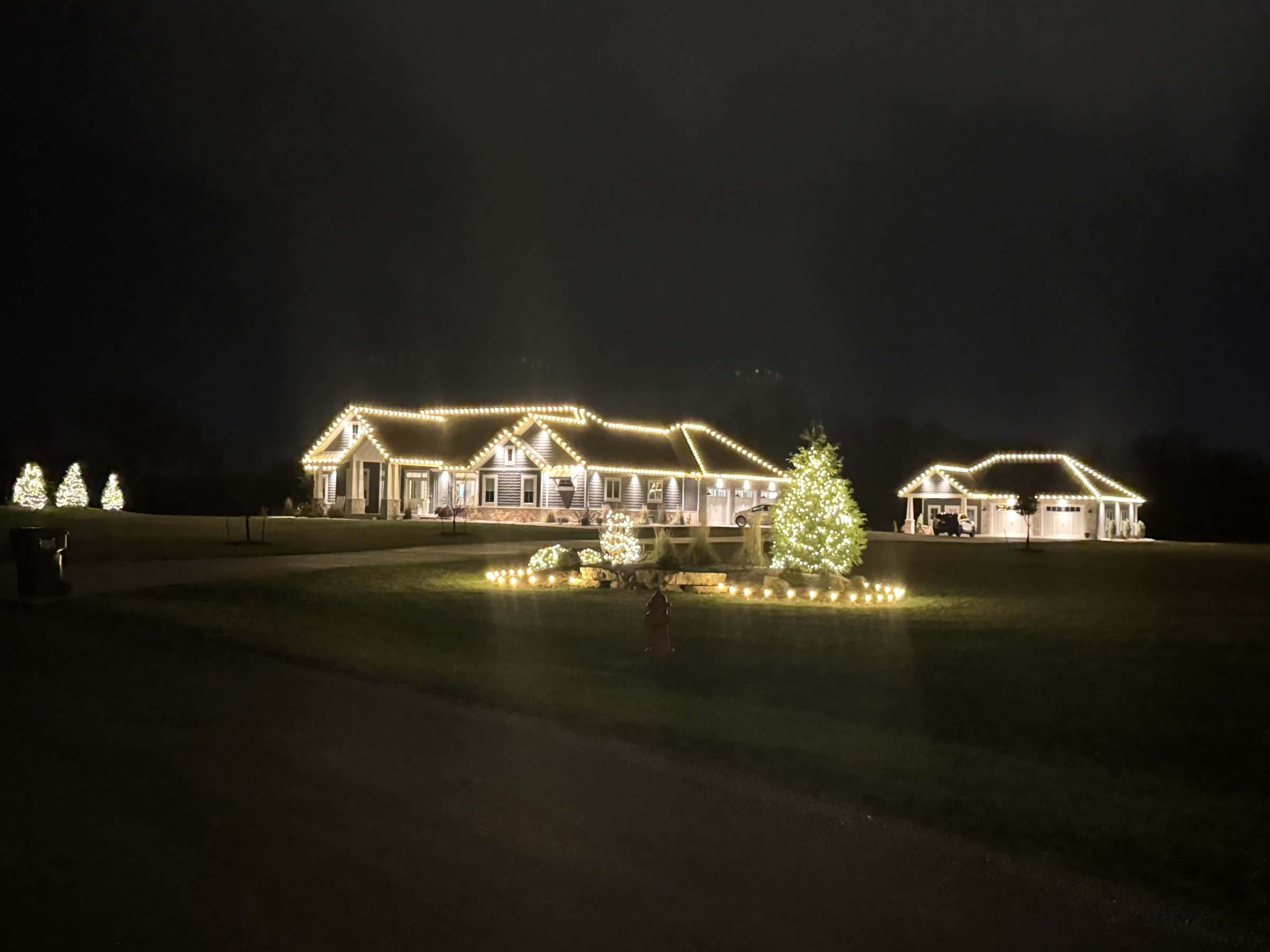 Ranch home and detached garage with warm white roofline lights and wrapped trees, the kind of display we remove and store in January