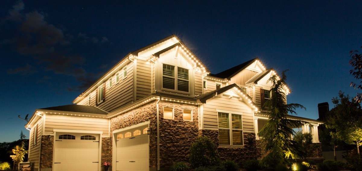 Two-story stone and siding home with a custom-designed warm white roofline lighting layout on every gable and dormer