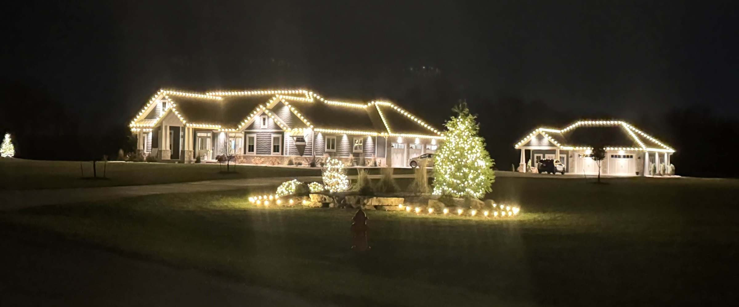 Warm white C9 Christmas lights professionally installed along the roofline of a Central Illinois ranch home with wrapped evergreen trees