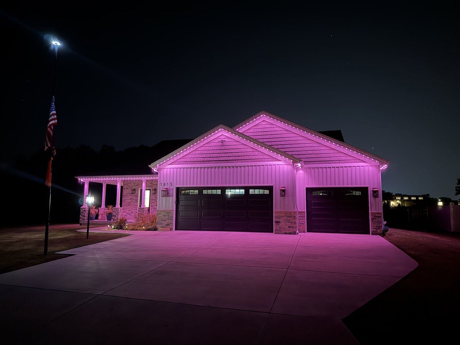 Permanent roofline lighting glowing pink on a garage and covered porch with a flagpole in the foreground