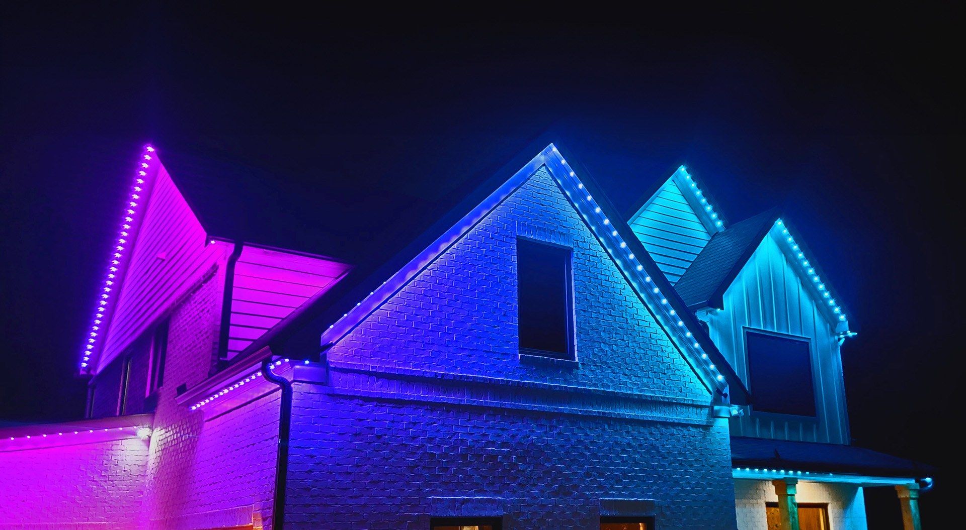 Permanent color-changing roofline lights in purple and blue on a brick home at night