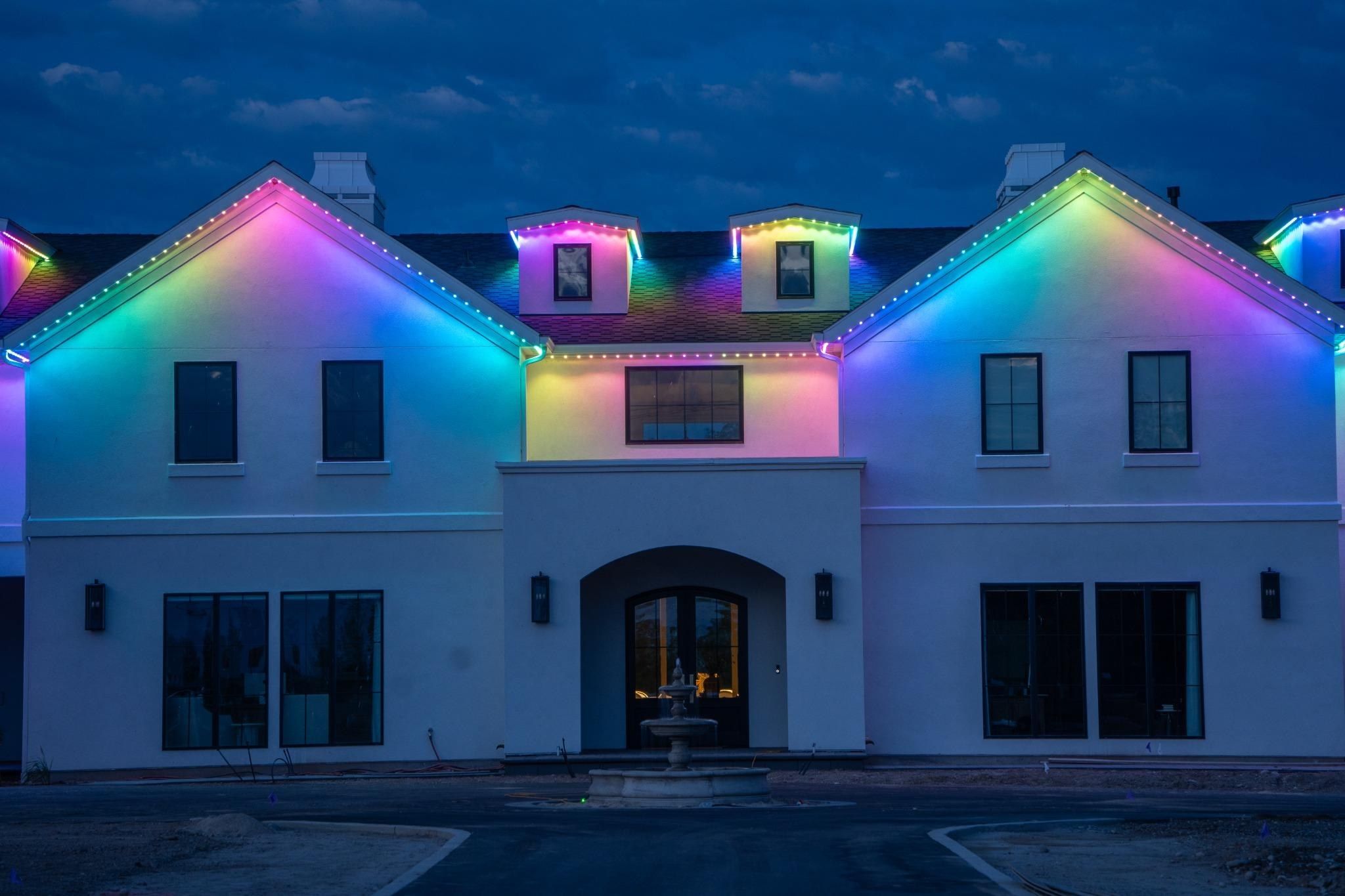 White two-story home with permanent lights cycling through a rainbow gradient along the roofline and dormers